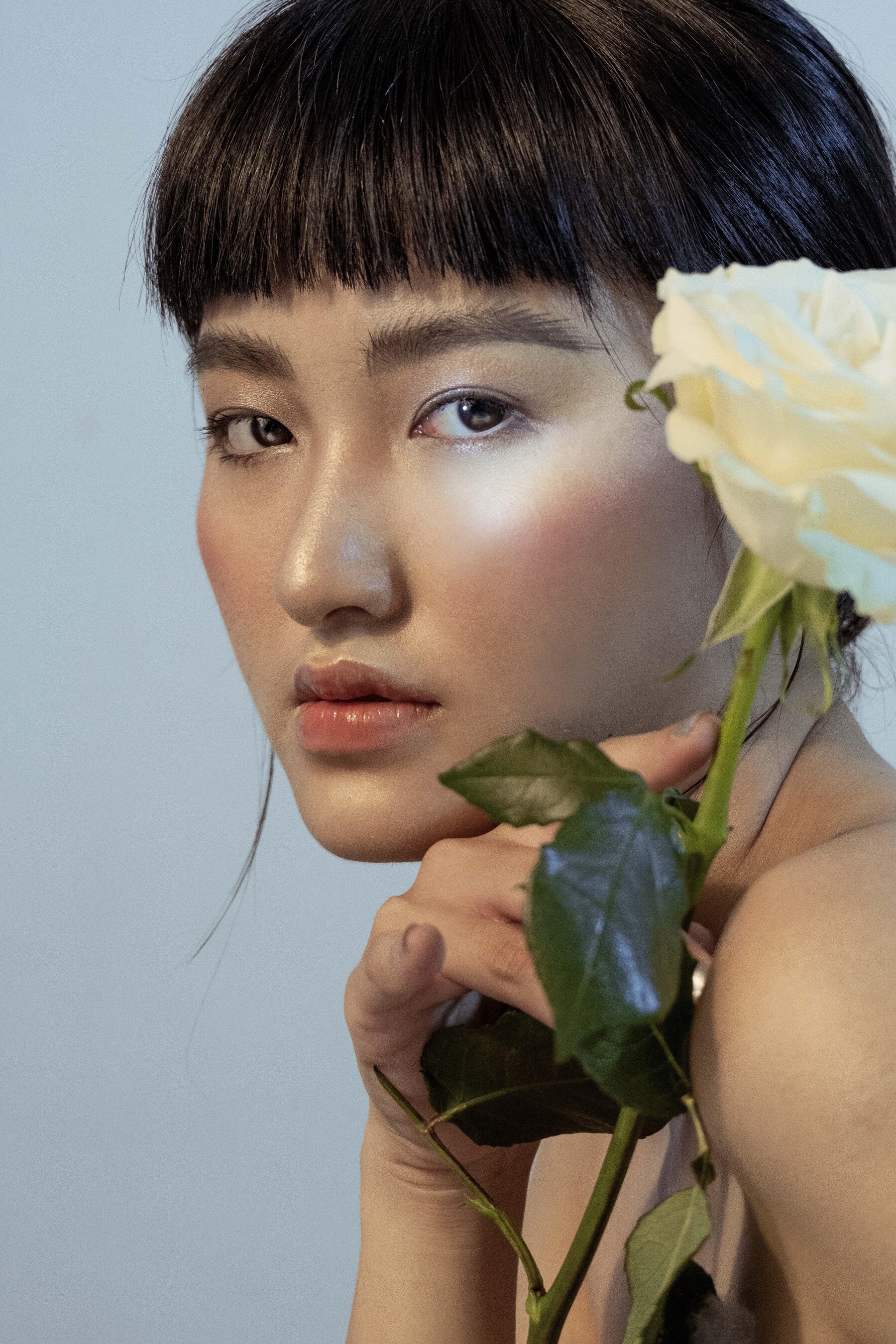 Portrait of an Asian woman holding a white rose with luminous-looking skin